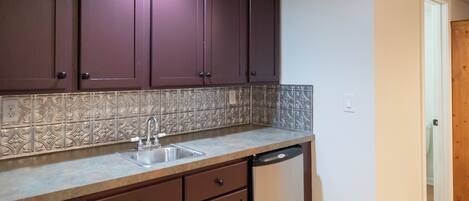A kitchen with dark brown cabinets, a tiled backsplash, a stainless steel sink, and a dishwasher.