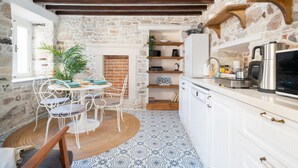 A rustic kitchen with exposed stone walls, a round dining table with chairs, and a built-in oven. - Miniq 101 - Near Sea & Foça Center Stone House (Izmir)