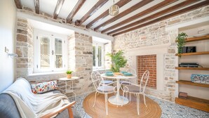 A cozy room with a stone wall, a fireplace, a round table with chairs, a sofa with a patterned cushion, and a bookshelf. - Miniq 101 - Near Sea & Foça Center Stone House (Izmir)