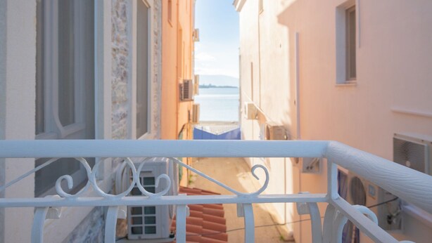 A narrow street with buildings on either side, a balcony railing in the foreground, and a view of the sea in the background. - Miniq 101 - Near Sea & Foça Center Stone House (Izmir)