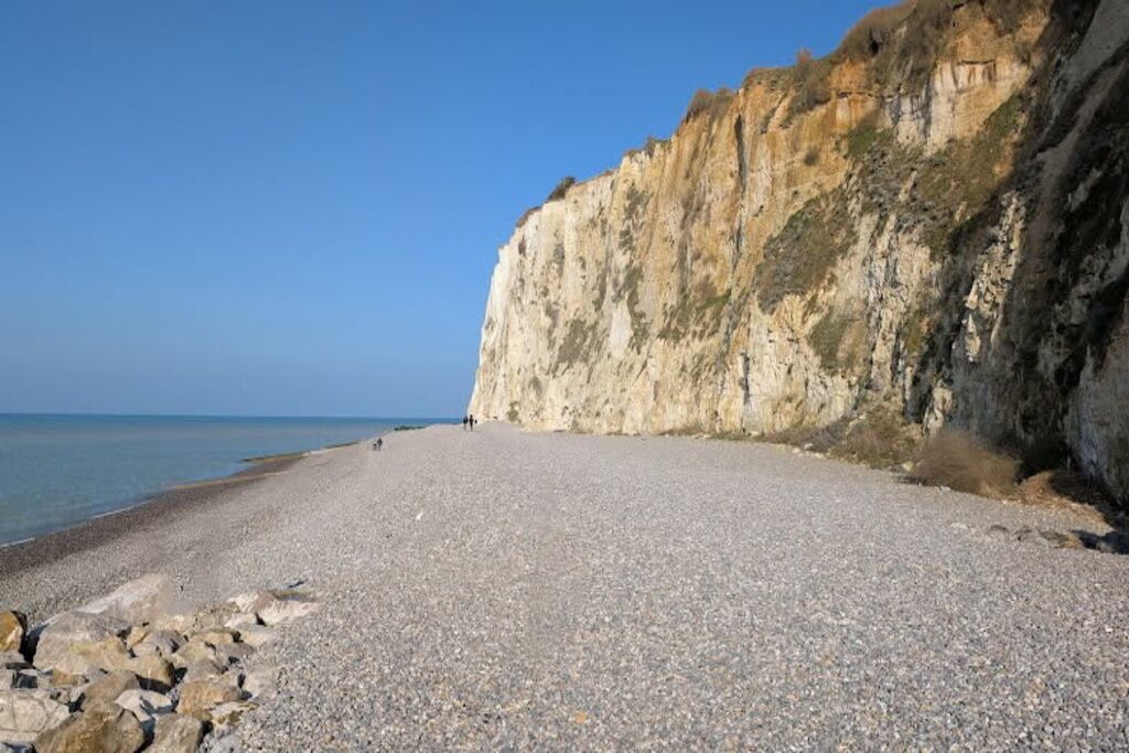 Ein Kiesstrand mit felsiger Küste und Klippen im Hintergrund.