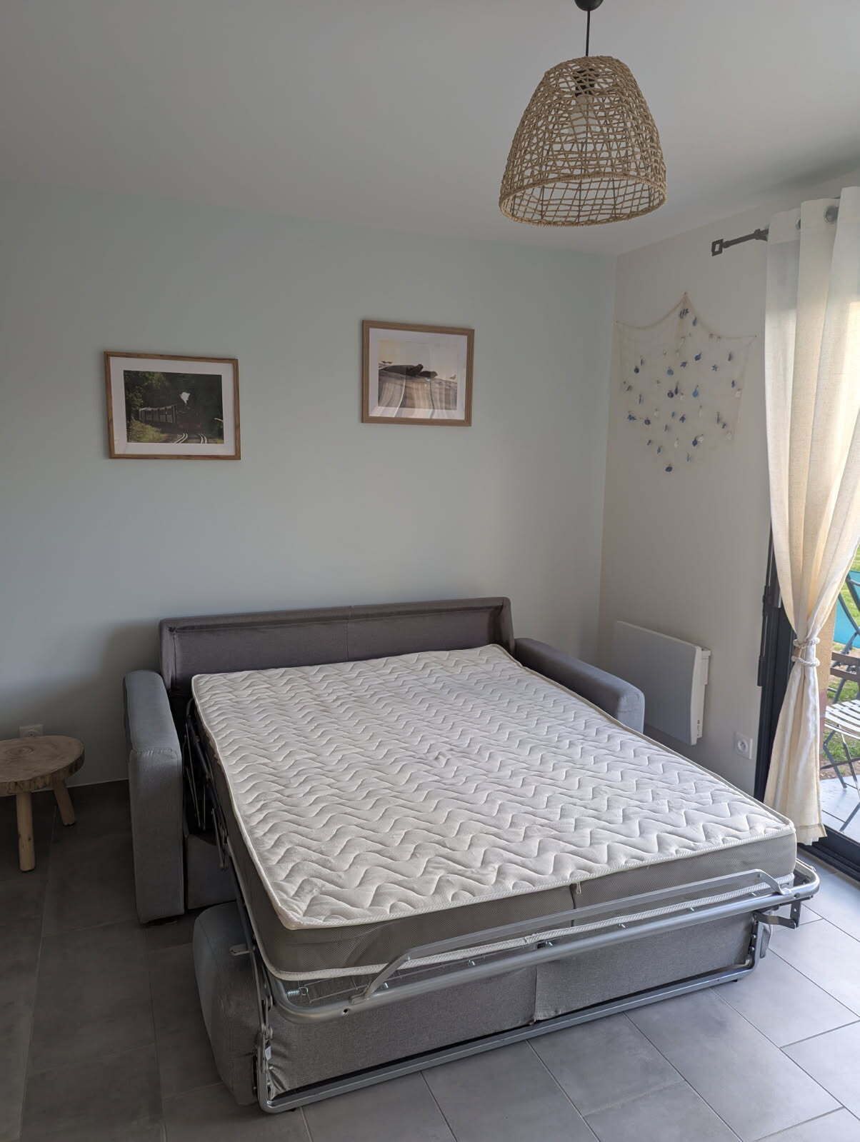 Een kleine slaapkamer met een uitschuifbed, een klein rond tafeltje en twee ingelijste foto's aan de muur.