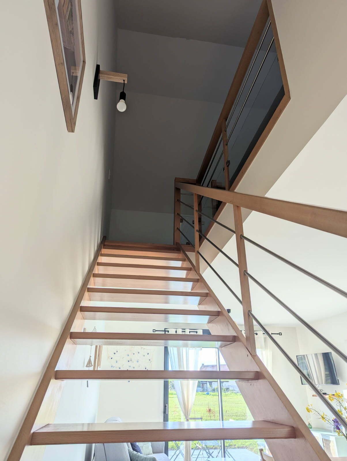 Eine moderne Treppe mit Holläufungen und Glasfeldern, die zu einem Außenbereich mit Blick auf einen Garten und ein Gebäude führt.