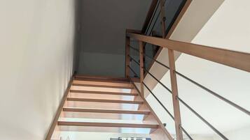 Eine moderne Treppe mit Holläufungen und Glasfeldern, die zu einem Außenbereich mit Blick auf einen Garten und ein Gebäude führt.