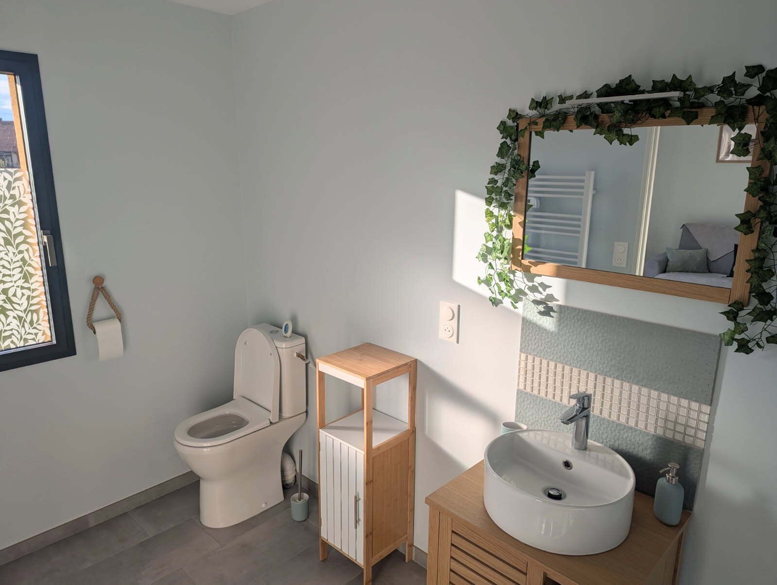 Ein modernes Badezimmer mit Toilette, einem Holz-Waschtisch, einem Waschbecken und einem Spiegel mit dekorativem Efein.