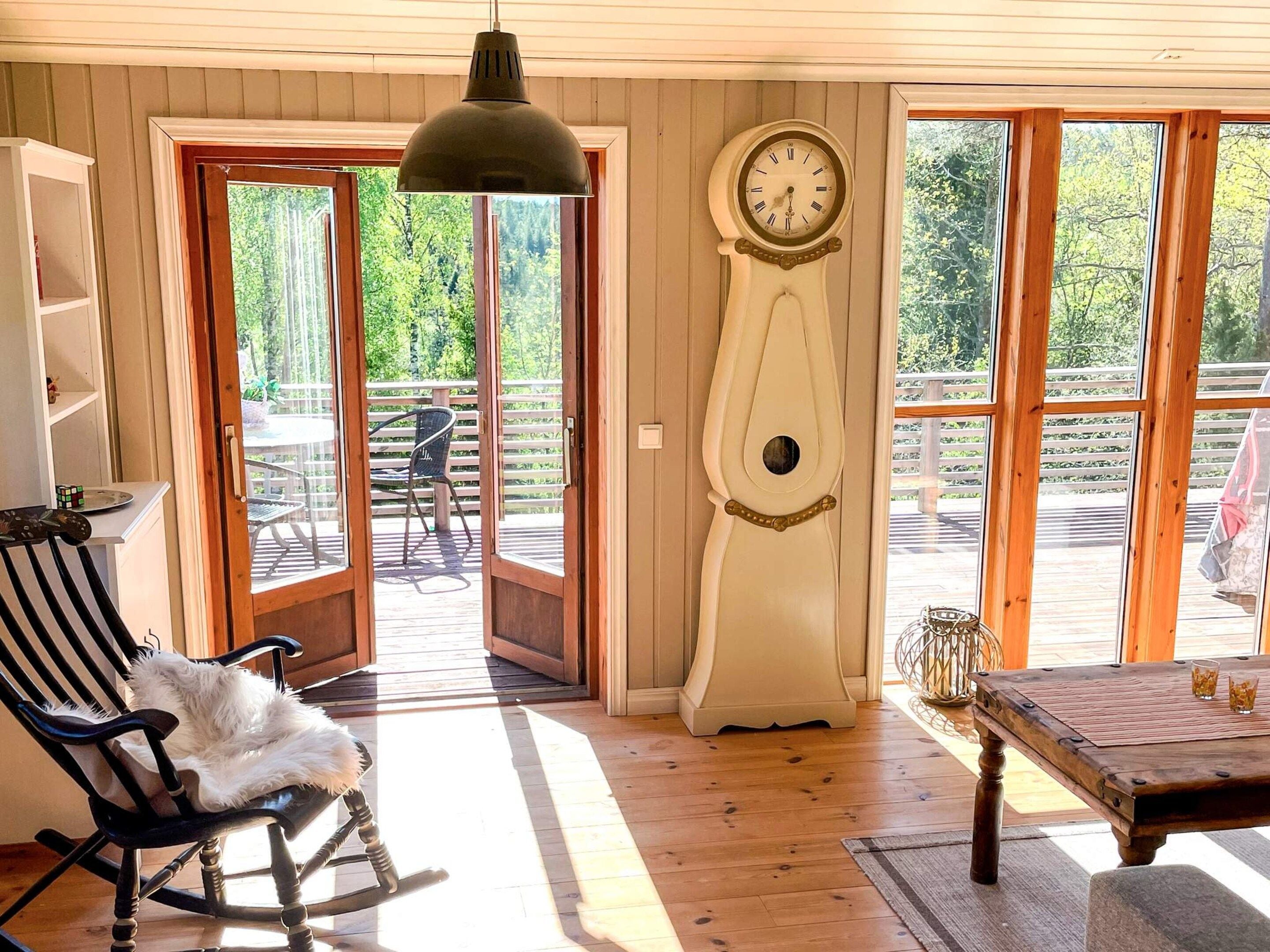 Una habitación con una mecedora, una mesa con vasos, un reloj y vistas a una terraza exterior a través de una puerta.