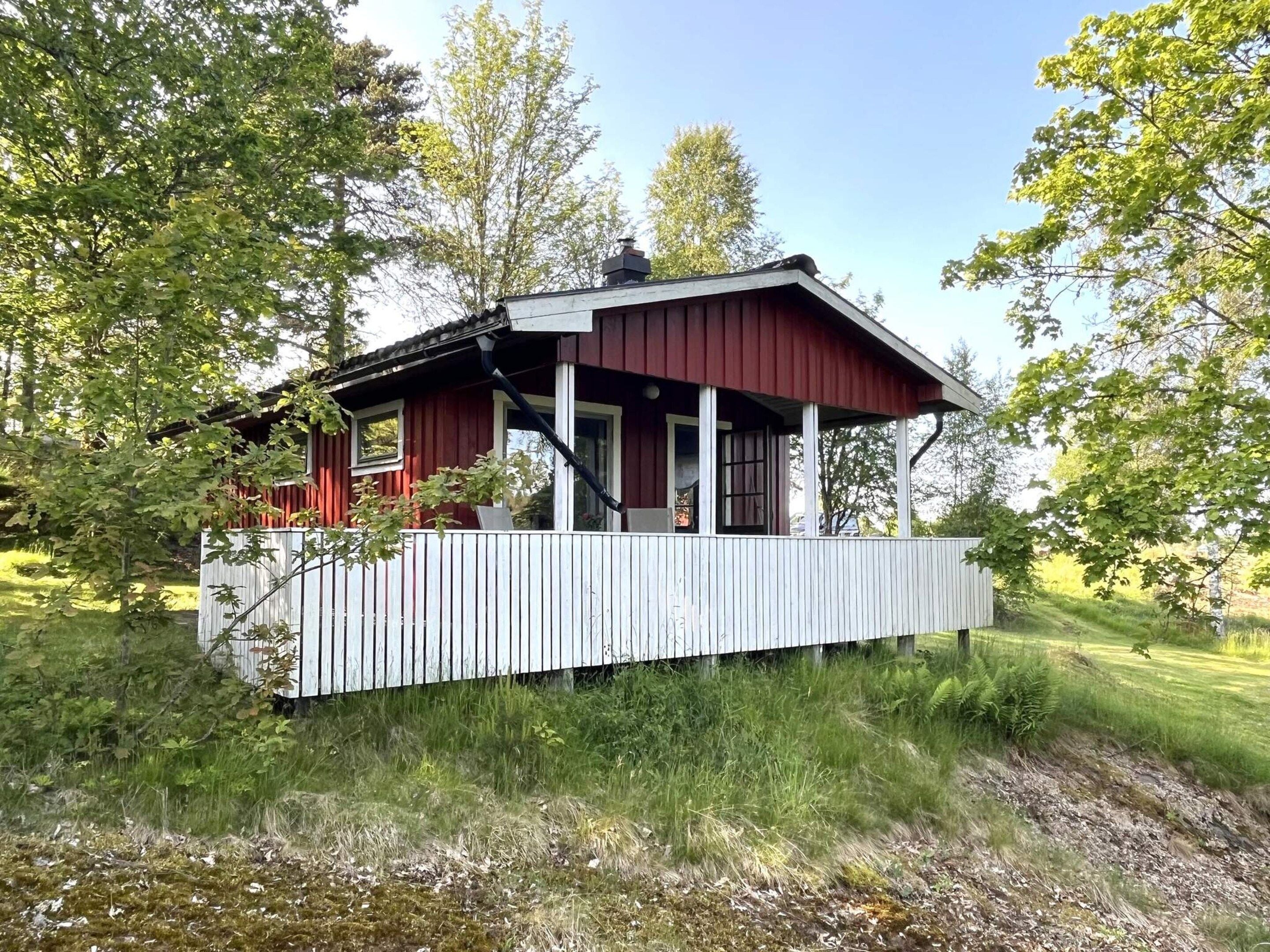 A red wooden cabin with a white porch, surrounded by trees and grass.