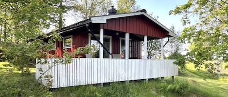 A red wooden cabin with a white porch, surrounded by trees and grass.