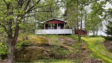 Uma cabana com um deck branco, cercada por árvores e uma área gramada.
