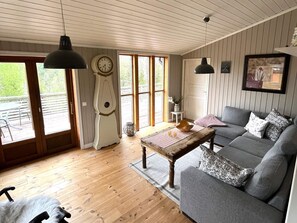 A cozy living room with a wooden floor, a grey sofa, a wooden coffee table, and a large window with a view of greenery. - 4 Star Holiday Home in Ed (Ed)