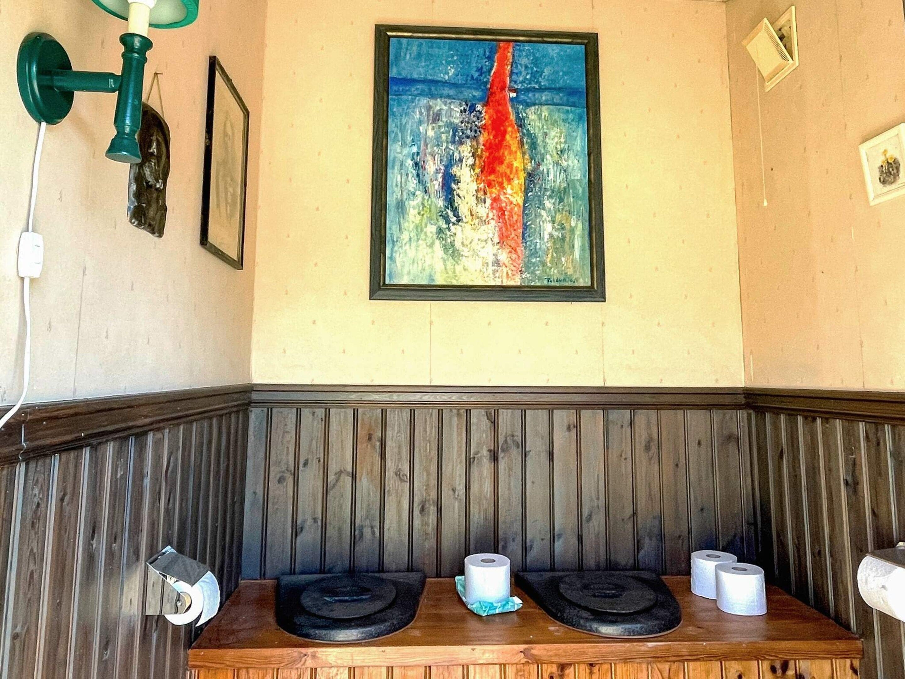 Una habitación con un banco de madera, un cuadro en la pared y una lámpara fijada a la pared.