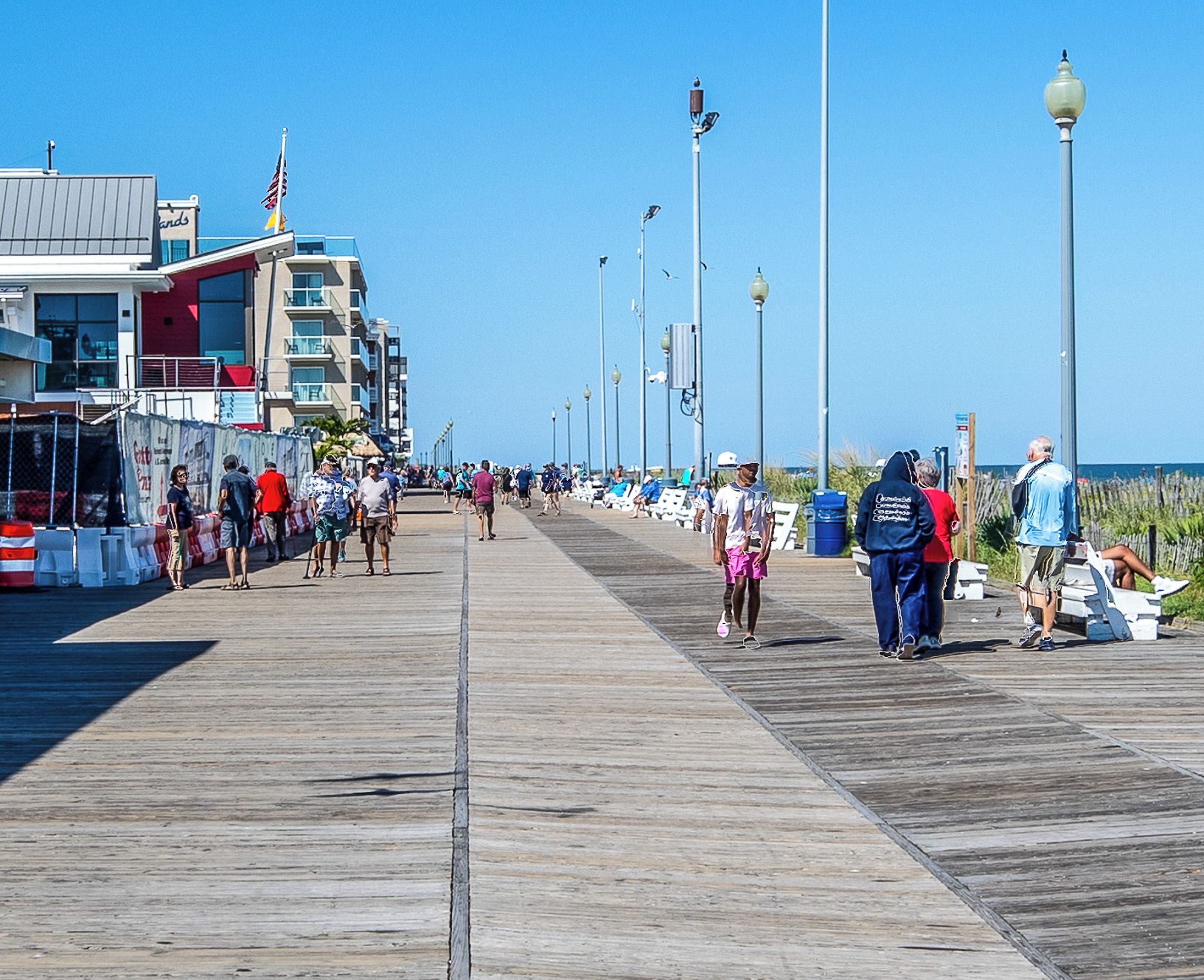 A boardwalk with people walking, a building with a sign, and street lamps.