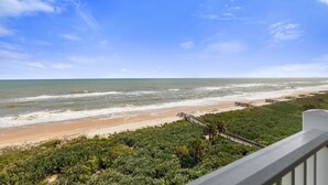 A beach view with a wooden walkway leading to the shore, surrounded by greenery. - Renovated top floor direct oceanfront penthouse Cinnamon Beach condo 862! (Palm Coast)