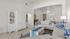 A spacious living room with a white sofa, a coffee table, and a white cabinet with glass doors. - Renovated top floor direct oceanfront penthouse Cinnamon Beach condo 862! (Palm Coast)