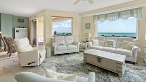 A living room with a view of the ocean, a ceiling fan, and a white sofa.