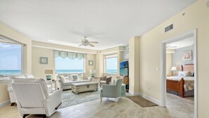 A spacious living room with a large window, a ceiling fan, and a view of the ocean.