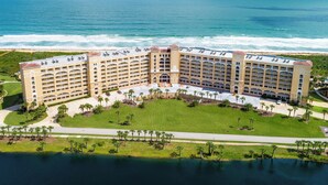 A large hotel with multiple floors and a central courtyard, surrounded by a body of water and a beach.