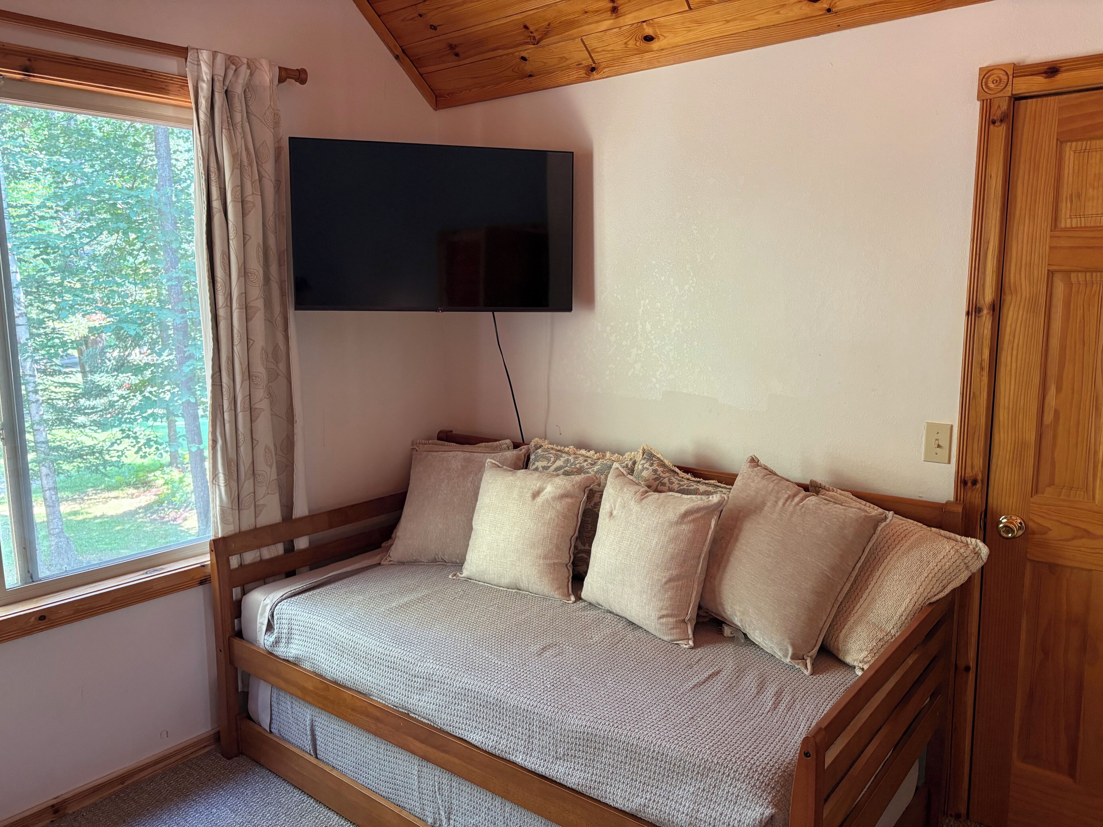 A cozy room with a wooden bed, a flat-screen TV mounted on the wall, and a window with curtains.