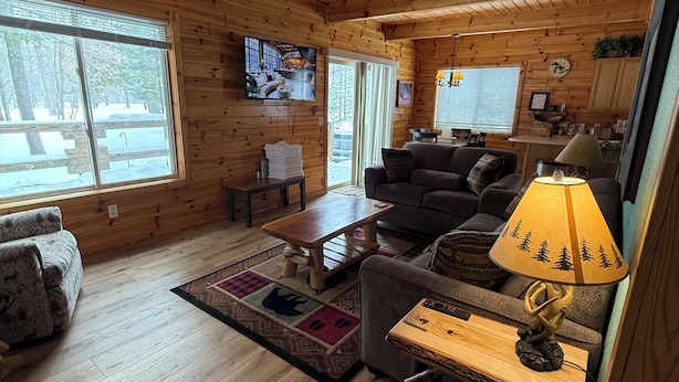 A cozy cabin interior with wooden walls and floors, a sofa, a coffee table, a TV, and a lamp. - Chalet at Thunder Bay Hot tub Pontoon Boat Pet friendly (Hillman)