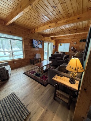 A cozy cabin interior with wooden walls and floors, a sofa, a coffee table, a TV, and a lamp.