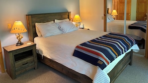 A neatly made bed with a striped blanket, two bedside lamps, a wooden nightstand, and a large mirror on the wall. - Chalet at Thunder Bay Hot tub Pontoon Boat Pet friendly (Hillman)