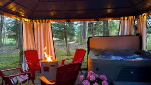 A hot tub with a fire feature, red chairs, and a potted plant with pink flowers. - Chalet at Thunder Bay Hot tub Pontoon Boat Pet friendly (Hillman)