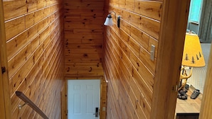 A narrow wooden hallway with a skylight, a white door at the end, and a small table with a lamp and remote control in the adjacent room. - Chalet at Thunder Bay Hot tub Pontoon Boat Pet friendly (Hillman)