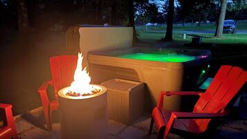 A hot tub with a fire feature, surrounded by red chairs, set on a paved patio.