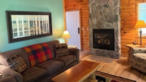 A cozy living room with a stone fireplace, wooden ceiling, and a blue wall. - Chalet at Thunder Bay Hot tub Pontoon Boat Pet friendly (Hillman)