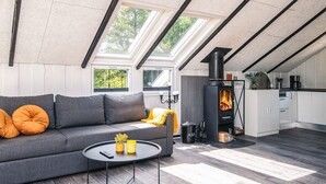 Un loft moderne avec un canapé gris, une table basse ronde et un coin cuisine équipé d’un poêle à bois.