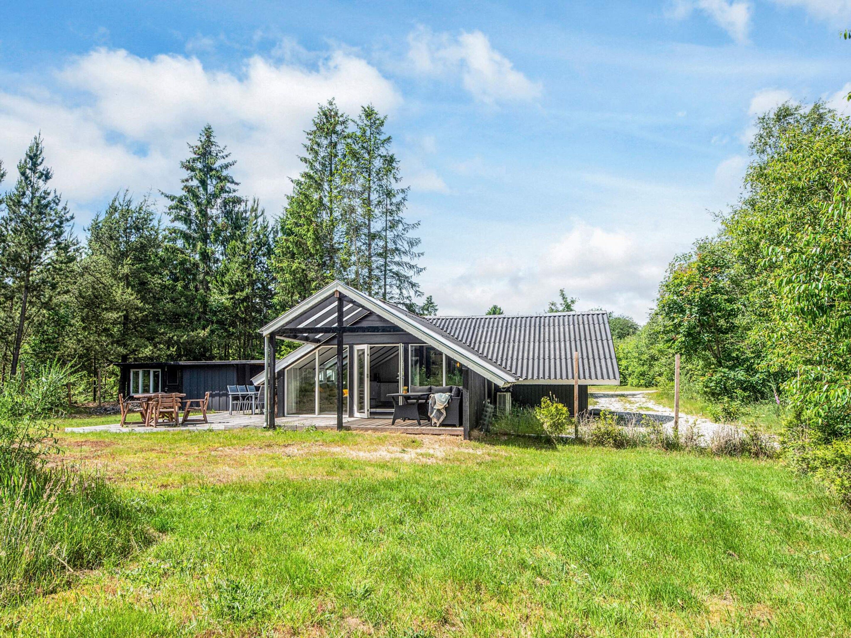 Una casa moderna con una terraza grande, rodeada de un bosque.