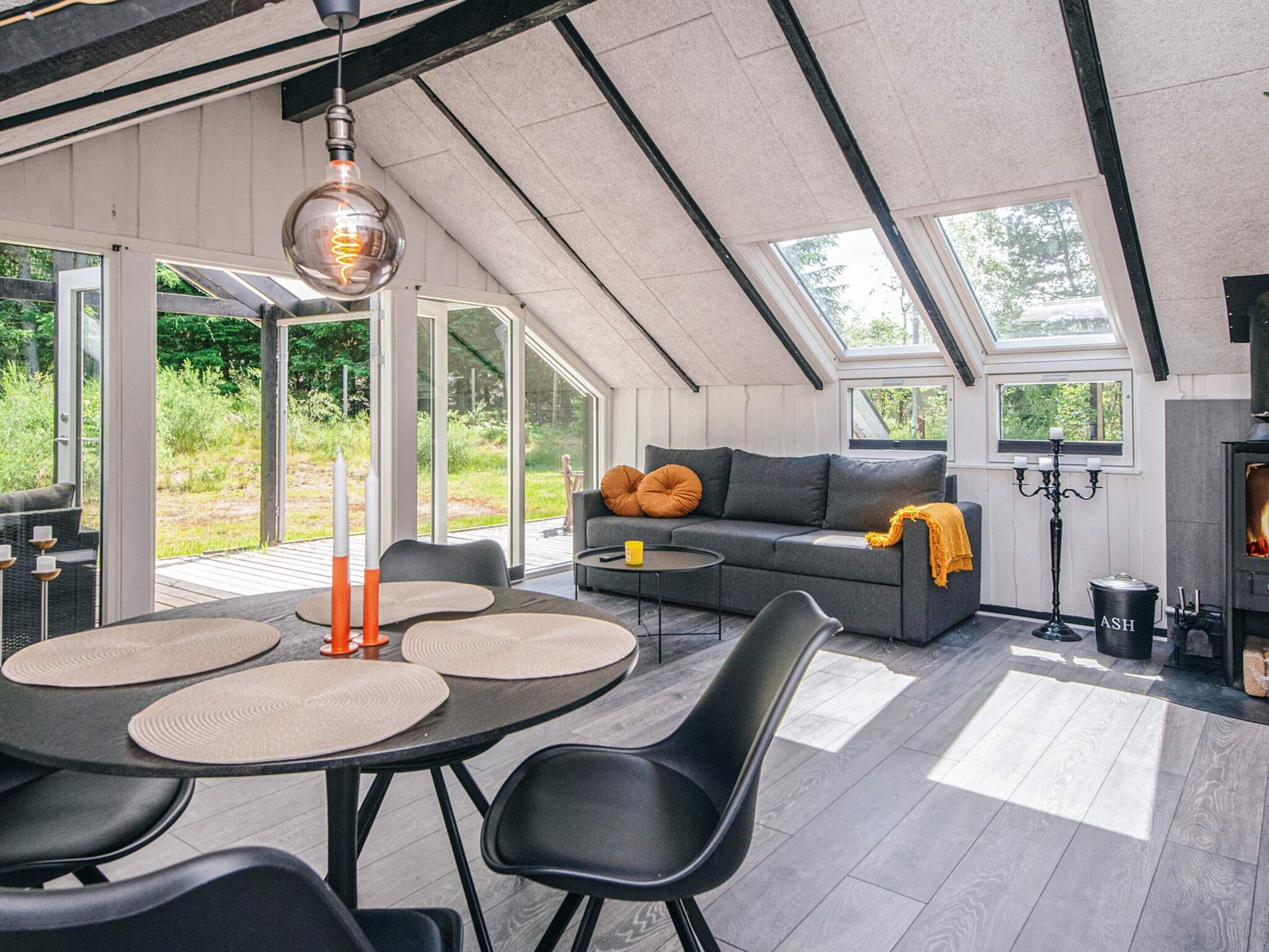 Un espacio habitable moderno estilo loft con techo alto, ventanas amplias, chimenea integrada y zona de comedor con mesas y sillas redondas.