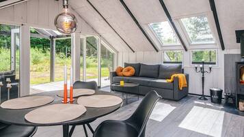 Un espacio habitable moderno estilo loft con techo alto, ventanas amplias, chimenea integrada y zona de comedor con mesas y sillas redondas.