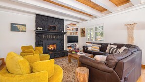 A cozy living room with a stone fireplace, a bookshelf, a leather sofa, and a yellow armchair. - Boujee Bear Lodge- BLS Access (Arnold)