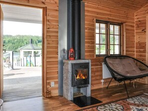 A wooden cabin interior with a stone fireplace, a black chair with a cushion, and a view of a dock and greenery outside. - 4 Star Holiday Home in Kil (Kil)