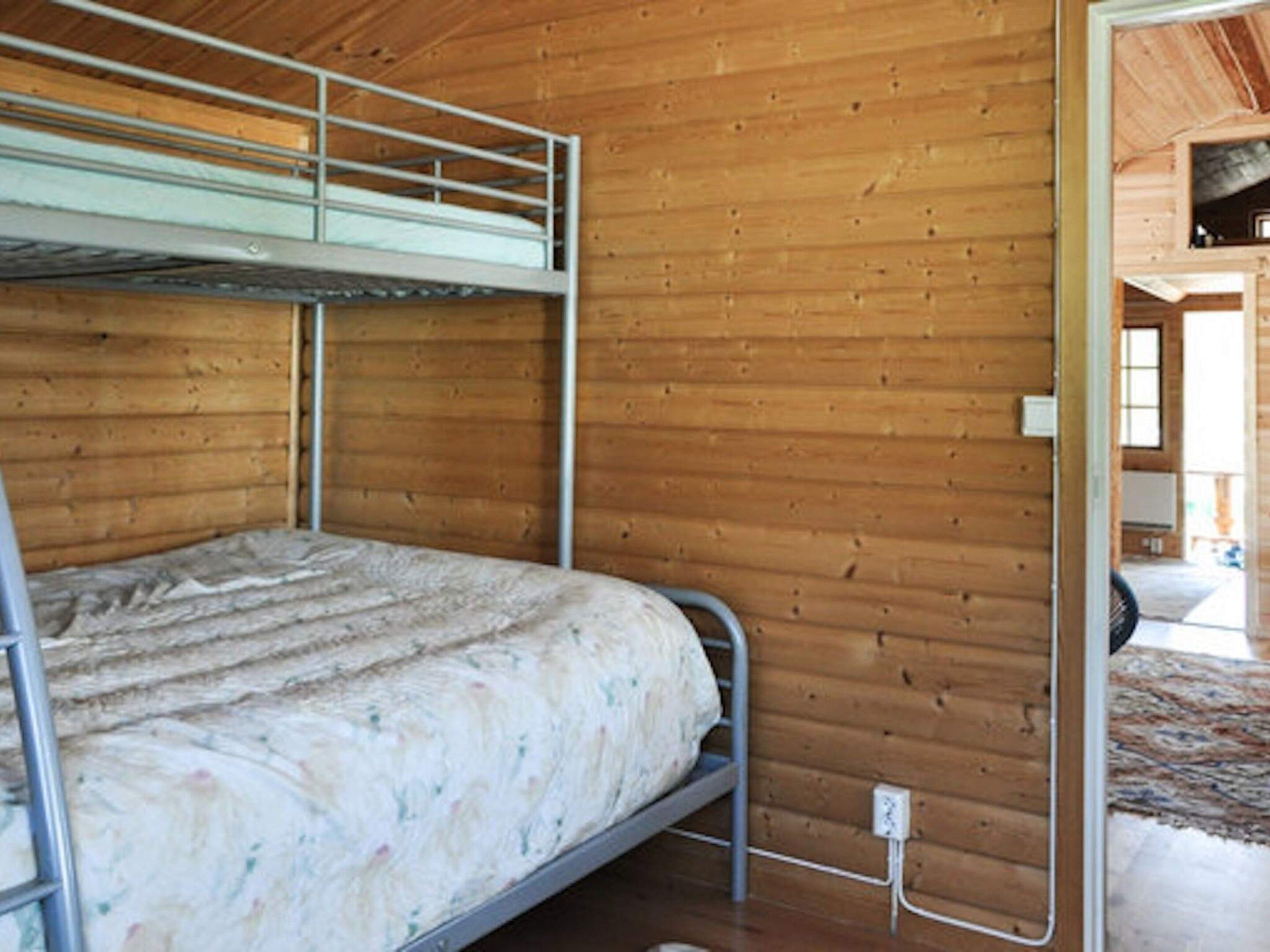 A bunk bed in a wooden room with a visible electrical outlet on the wall.