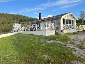A white cabin with a covered patio, surrounded by a gravel path and grassy area.