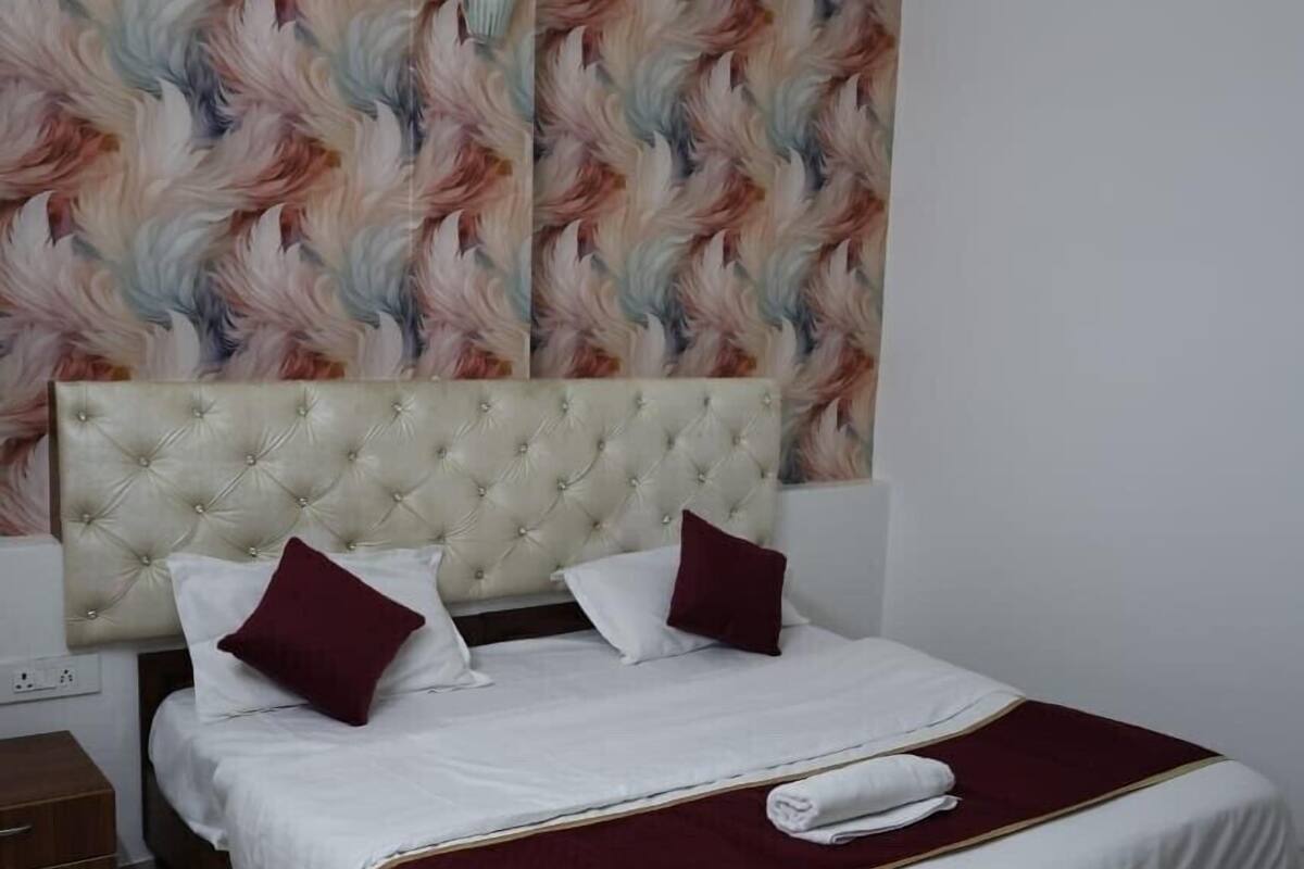 A neatly made bed with a tufted headboard, white linens, and a maroon throw blanket.
