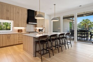 A modern kitchen with wooden cabinets, a large island with bar stools, and a view to the outdoor patio.