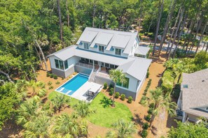 A modern house with a swimming pool, surrounded by palm trees and a well-maintained lawn.