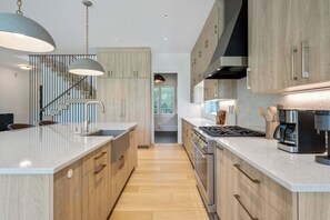 A modern kitchen with wooden cabinets, a central island, stainless steel appliances, and pendant lighting.