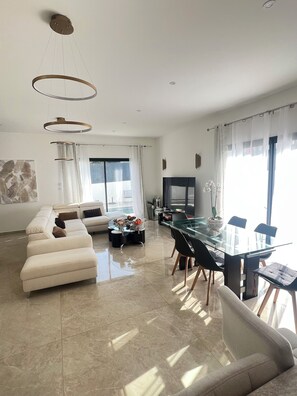 Een moderne woonkamer met een glazen eettafel, een bank en een televisie.