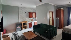 Ein gemütlicher Wohnraum mit einem grünen Sofa, einem kleinen Holztisch, einem Bett, einer Küchenzeile mit Schränken und einer Tür zu einem Badezimmer.