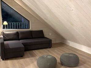 A modern loft bedroom with a dark grey sectional sofa, a large window with a view of trees, and a wooden floor. - 5 Star Holiday Home in Ugglarp (Sloinge)