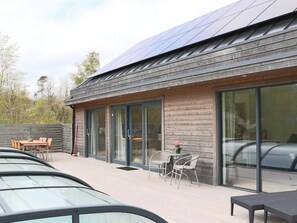 Een modern gebouw met grote glazen deuren, een terras met buitenmeubilair en een geparkeerde auto ervoor.