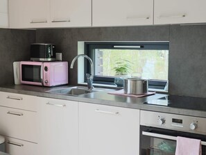 Une cuisine moderne avec un évier en acier inoxydable, un micro-ondes rose et une fenêtre donnant sur un paysage verdoyant.