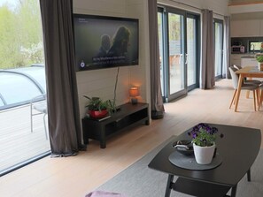 Un salon moderne avec un téléviseur à écran plat fixé au mur, un coin repas avec une table et des chaises, et un balcon avec une voiture garée à l’extérieur.