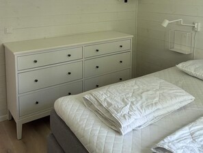 Une chambre à coucher avec un lit, une commode blanche dotée de nombreux tiroirs et une table de chevet avec une lampe.