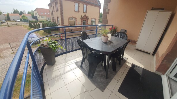 A balcony with a table and chairs, a potted plant, and a view of a building with a sign that reads "Café".