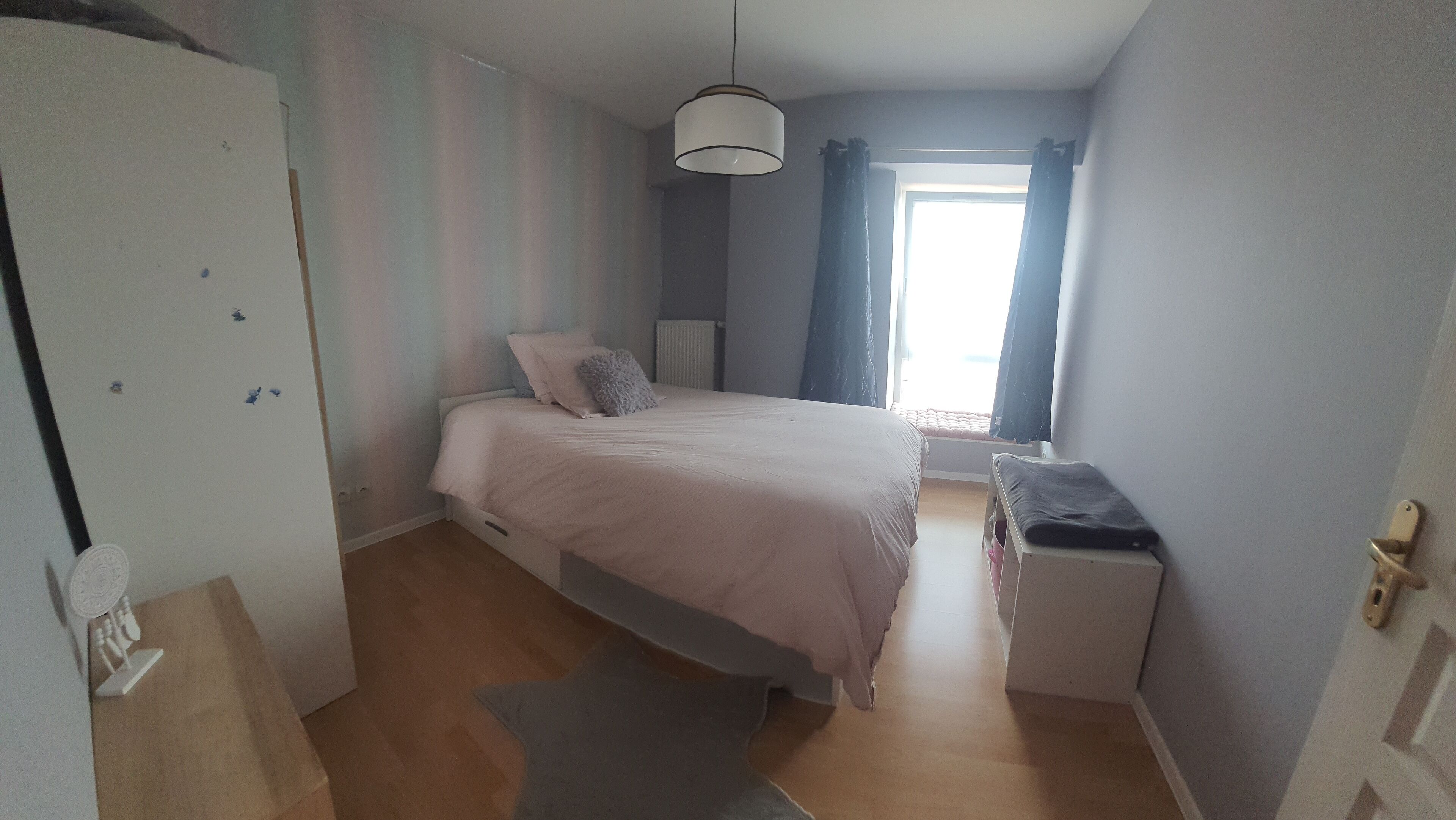 A bedroom with a bed, a wardrobe, a desk, and a window with curtains.